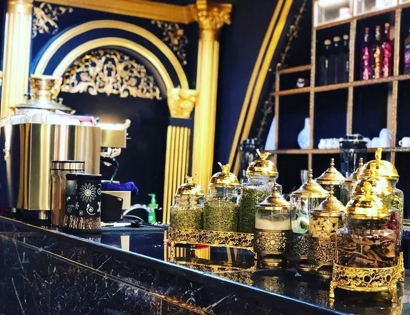 فضای داخلی مجلل رستوران وی آی پی کاظمی با دیوارهای آبی نفتی و تزئینات طلایی، نمایش انواع دمنوش و چای در ظروف لوکس طلایی.