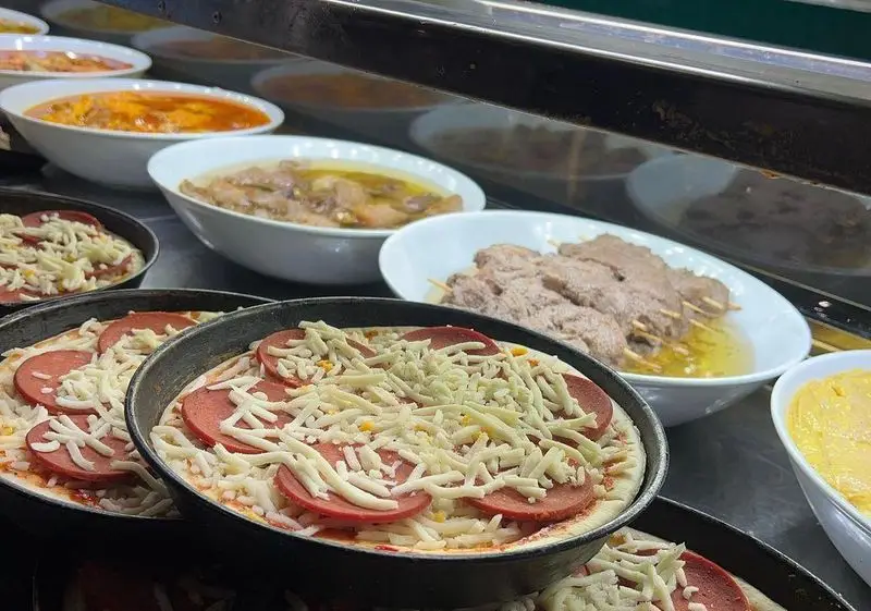 نمای نزدیک از انواع غذاهای آماده و خوشمزه در رستوران وی آی پی کاظمی شامل پیتزاهای آماده پخت با پپرونی و پنیر، کباب و خورش.