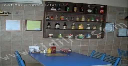 فضای داخلی دنج و چیدمان میز ناهارخوری در رستوران پیتزا آرد، با قفسه سس‌ها، بطری‌ها و قاب‌های روی دیوار کاشی‌کاری.