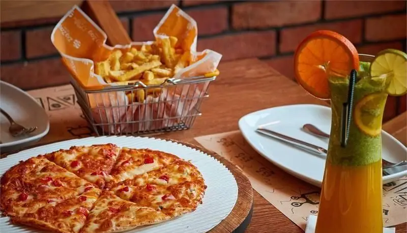 پیتزا زیگ زاگ تازه با پنیر و تکه های قرمز، به همراه سیب زمینی سرخ کرده در سبد و نوشیدنی میوه ای خنک در پیتزایی زیگ زاگ.