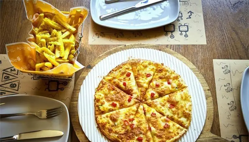پیتزایی زیگ زاگ: یک پیتزای جذاب با پنیر و فلفل دلمه‌ای، همراه با سیب‌زمینی سرخ‌کرده در بسته‌بندی خاص زیگ زاگ روی میز رستوران.