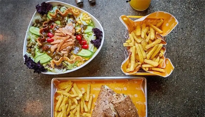 نمای بالایی از میز غذای پیتزایی زیگ زاگ: سالادی رنگارنگ، سیب زمینی سرخ کرده، ساندویچ و نوشیدنی.