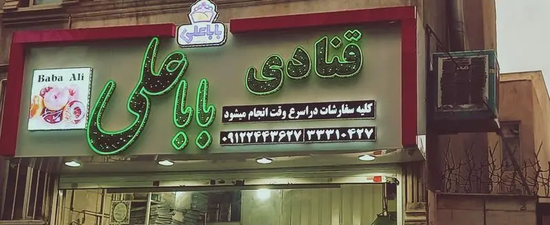 تابلوی روشن قنادی "باباعلی"، ارائه‌دهنده پیراشکی و کیک یزدی، با لوگو، تصویر دونات و شماره‌های تماس برای سفارشات.
