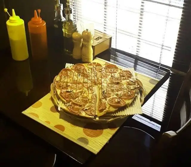 پیتزای بزرگ و جذاب رستوران ایتالیایی اسی فود روی میز با سس و ادویه‌جات. تجربه‌ای دلنشین از غذای ایتالیایی در محیطی آرام.