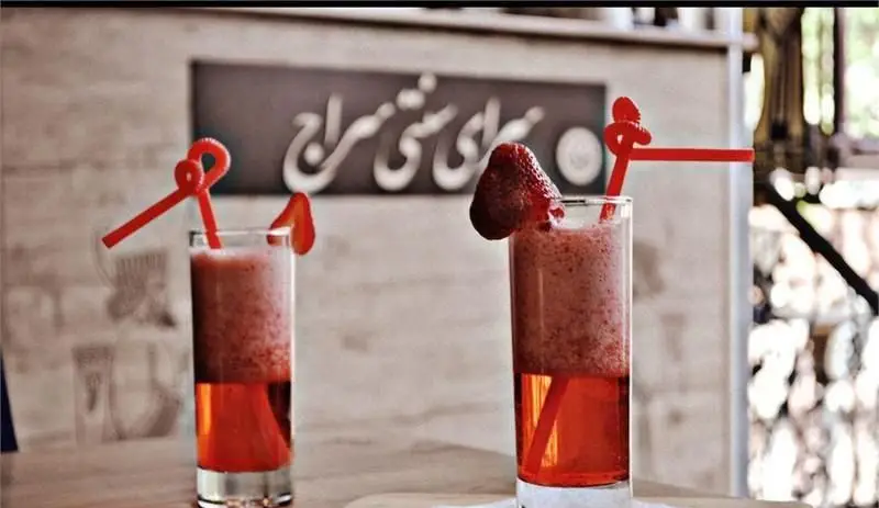 دو لیوان نوشیدنی خنک توت فرنگی لایه‌ای با اسموتی، نی و توت فرنگی تازه در کافه رستوران سنتی سراج، انتخابی ایده‌آل برای تابستان.