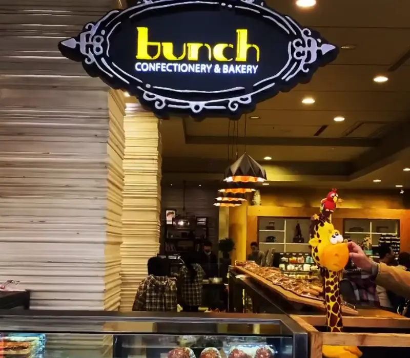 نمای داخلی بوتیک نان و شیرینی بانش با تابلو روشن "Bunch Confectionery & Bakery" و محصولات تازه قنادی و پخت روز.