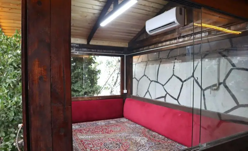 فضای داخلی دنج باغچه رستوران ونوس شهران با سقف چوبی، تخت‌های سنتی قرمز، قالیچه زیبا و تهویه مطبوع، مشرف به فضای سبز.