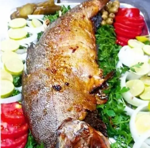 ماهی کباب تازه و خوشمزه از رستوران ایرانی خوتکا، غذای سنتی دریایی ایرانی با سبزیجات معطر و لیمو، آماده برای سرو.