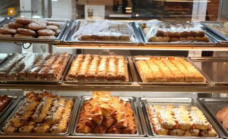 تصویری از ویترین جذاب و پربار نان و شیرینی تهران با انواع شیرینی، باقلوا، کلوچه و رولت‌های تازه و دلپذیر.