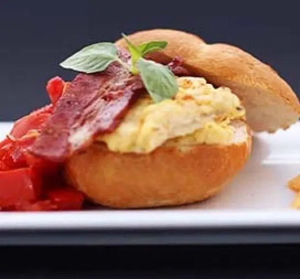 صبحانه ویژه ویونا پلاس: نان گرد پر از تخم مرغ همزده، بیکن ترد، سبزیجات تازه و برگ ریحان. غذایی دلپذیر در کافه رستوران ویونا پلاس.