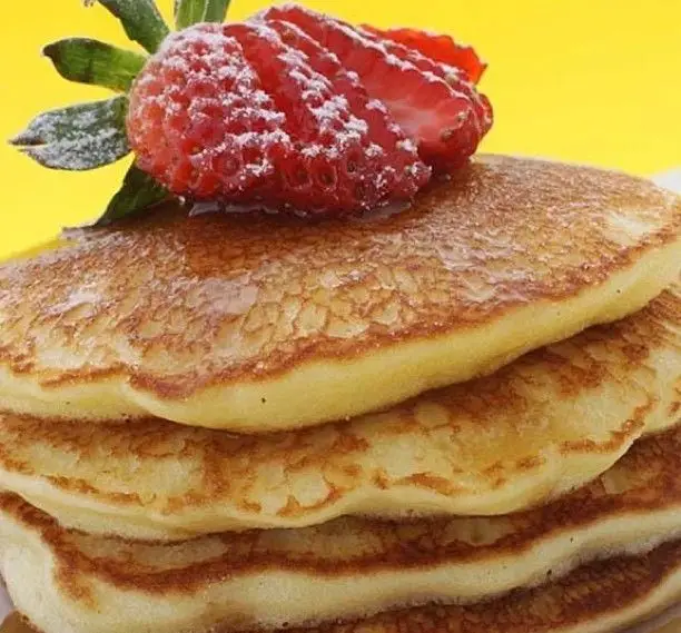 تصویر دلپذیر از پنکیک‌های طلایی با شربت عسل، توت فرنگی تازه و پودر قند در کافه رستوران ویونا پلاس، ایده‌آل برای یک صبحانه فراموش‌نشدنی.