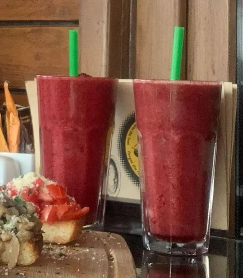 تصویری از دو اسموتی میوه‌ای قرمز با نی سبز و پیش‌غذاهای جذاب بروشتا (گوجه و قارچ) در کافه رستوران ویونا پلاس. لذت نوشیدنی خنک.