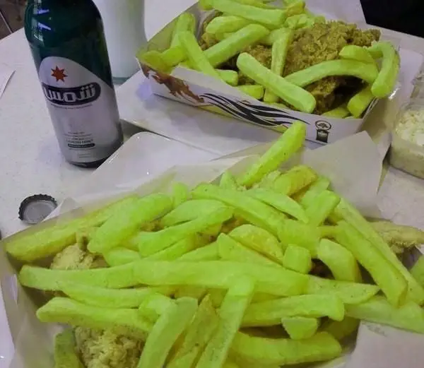 تصویری از یک وعده فست فود کامل در رستوران دراگون، شامل سیب زمینی‌های سرخ کرده سبز رنگ و ترد سوخاری به همراه نوشیدنی شمس.