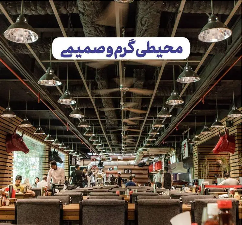 فضای داخلی رستوران ته دیگ، محیطی گرم و صمیمی با دکوراسیون مدرن و نورپردازی دلنشین. مشتریان در حال صرف غذا در فضایی با سقف بلند و فن‌های سقفی.