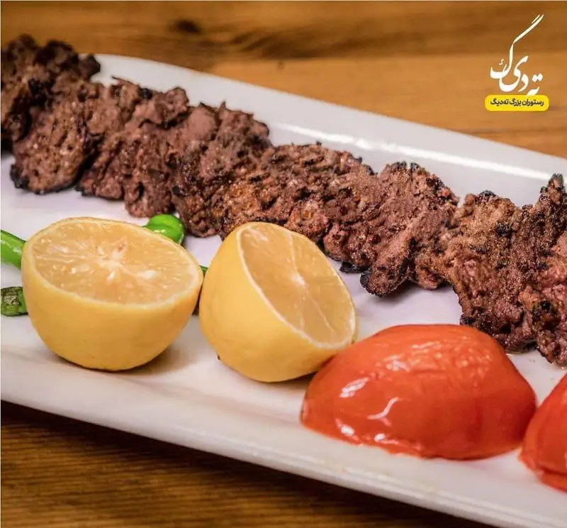 تصویر جذاب کباب کوبیده لذیذ رستوران ته دیگ با برش‌های لیمو، گوجه و فلفل کبابی. تجربه طعم اصیل ایرانی.
