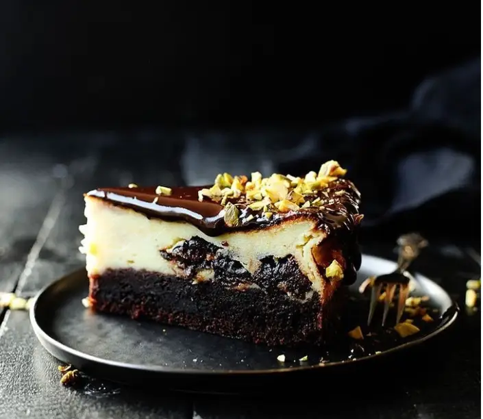 یک برش چیزکیک براونی شکلاتی با لایه میوه خشک یا شکلات، رویه گاناش و پسته خرد شده، دسر خاص کافه اودسا.