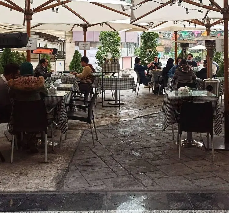 کافه رستوران نقطه سفید با فضای باز دنج و دلنشین، میز و صندلی‌های زیبا زیر چترهای سفید، پذیرای مشتریان برای صرف غذا و نوشیدنی.