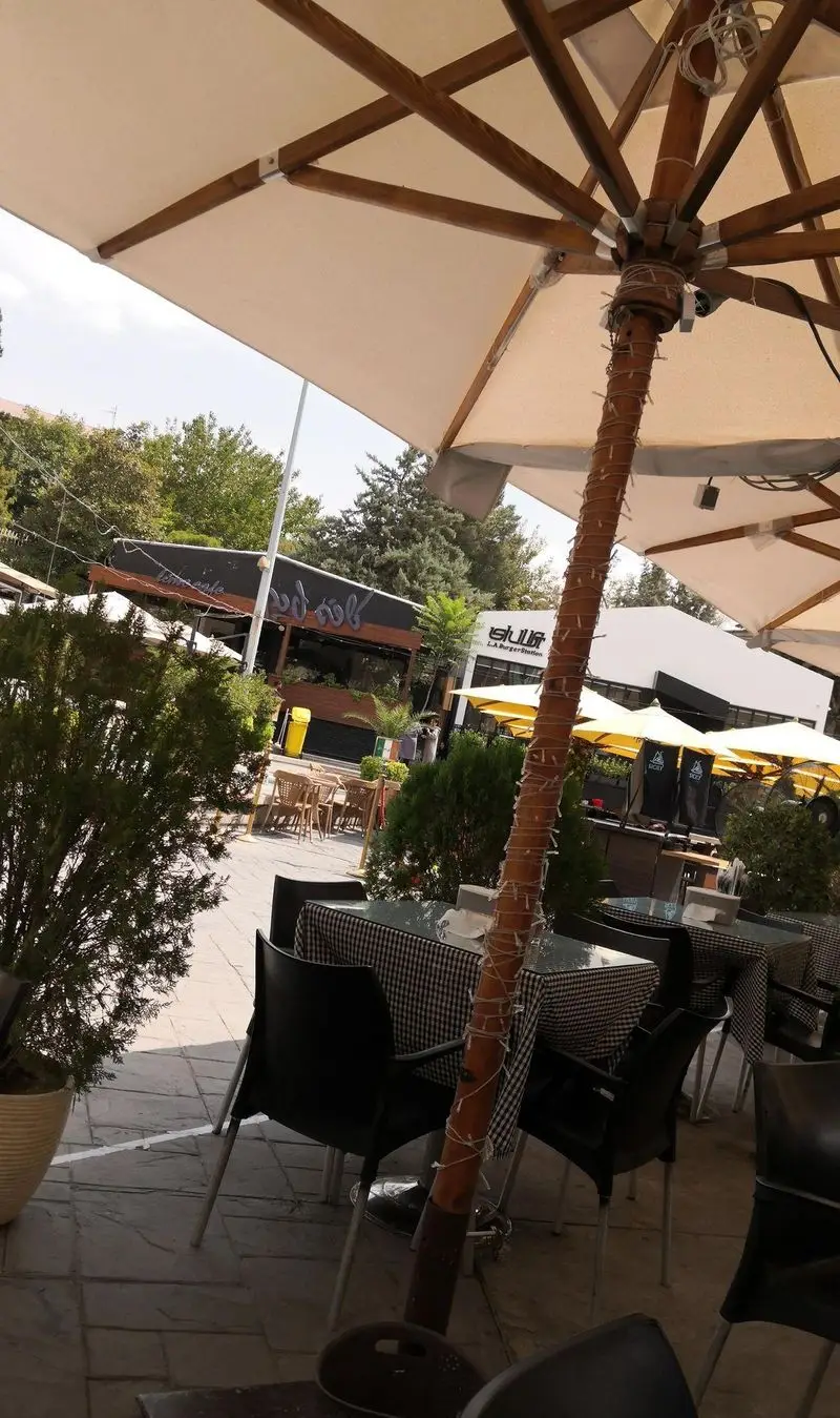 محیط دنج و زیبای فضای باز کافه رستوران نقطه سفید با چترهای بزرگ، میز و صندلی‌های راحت و دکوراسیون دلنشین.