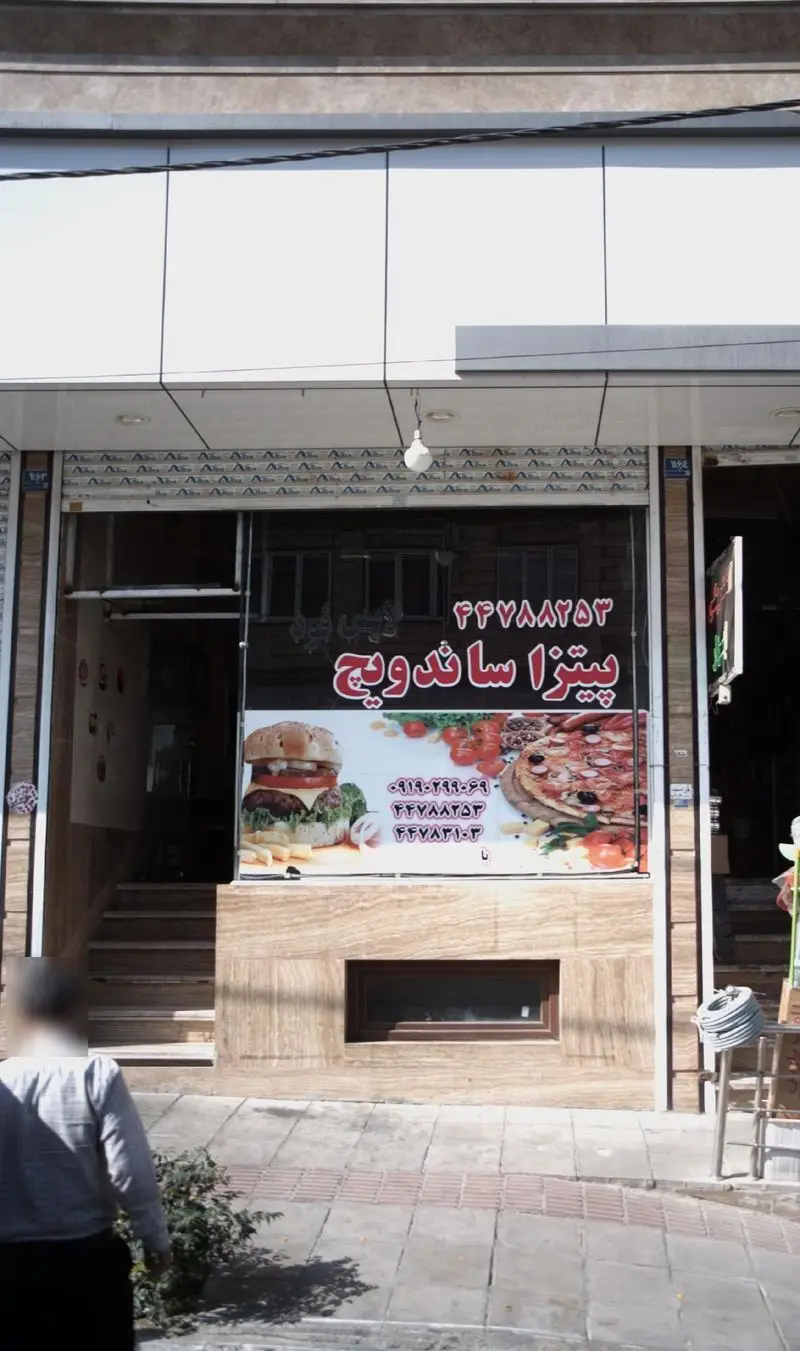 تصویر نمای بیرونی فروشگاه پیتزا و ساندویچ با تابلو روشن و تصاویر جذاب غذا مانند پیتزا، همبرگر و شماره تماس برای تحویل.