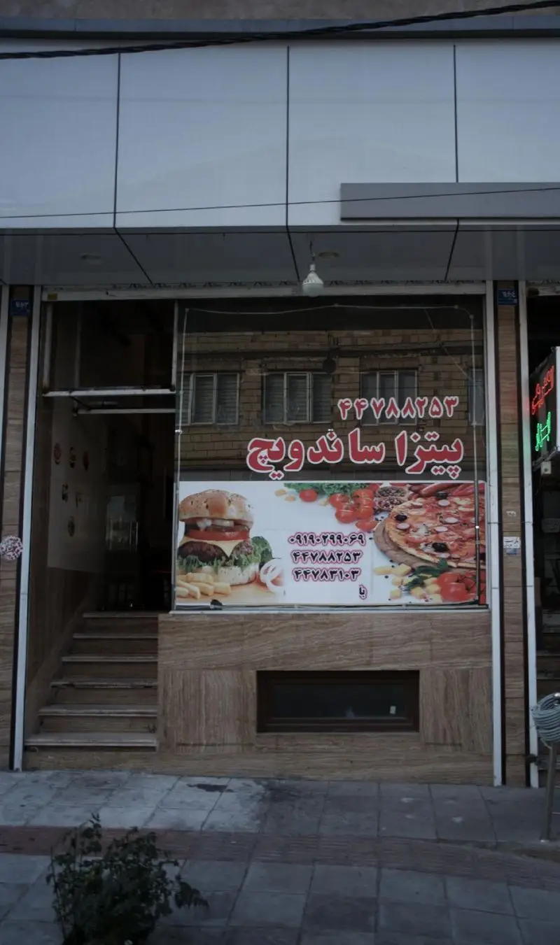نمای بیرونی فست فود پیتزا ساندویچ با تابلو و تصاویر پیتزاهای خوشمزه و ساندویچ‌های برگر، مناسب برای سفارش تلفنی و حضوری.
