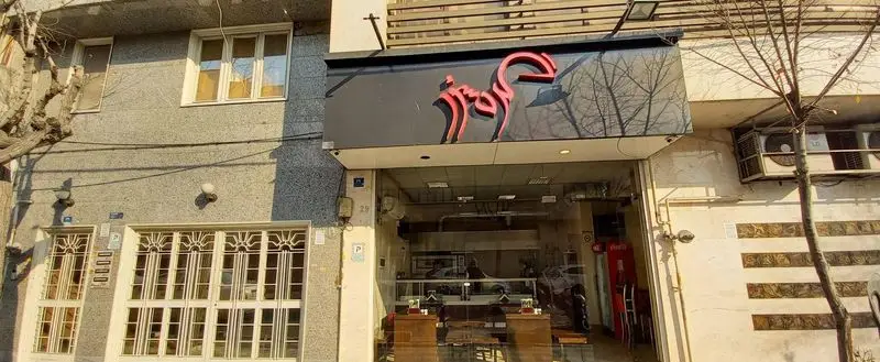 ورودی رستوران گردسوز با تابلو نام به رنگ قرمز و طراحی مدرن، بازتاب درختان در شیشه‌های ورودی. آماده پذیرایی از مشتریان.