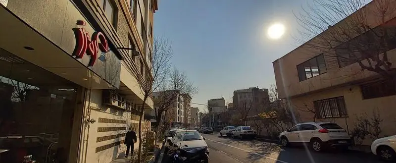 نمای بیرونی رستوران گردسوز در یک روز آفتابی با تابلوی قرمز، ساختمان‌های اطراف و خودروها در خیابان و پیاده‌رو.