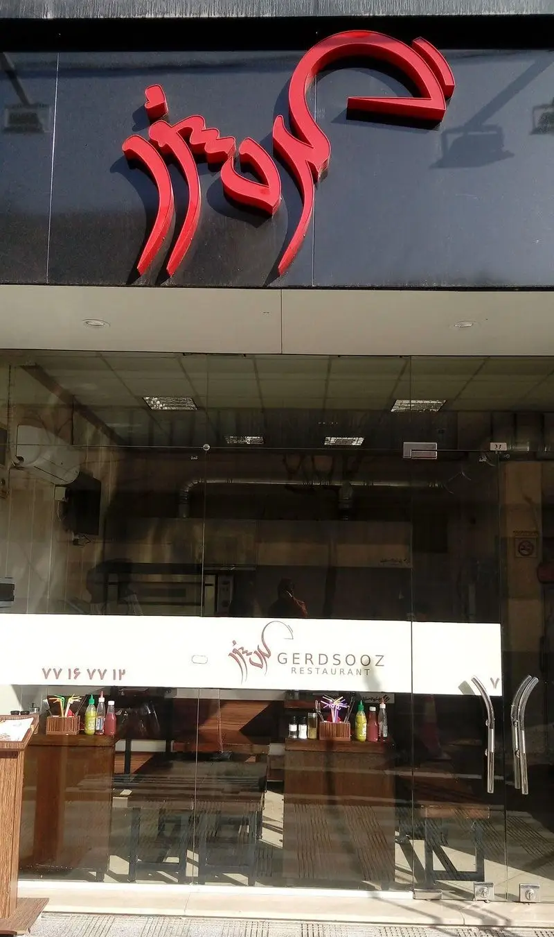 رستوران گردسوز: تصویری از نمای بیرونی با تابلوی بزرگ و برجسته قرمز رنگ، ورودی شیشه‌ای و میزهای داخلی قابل مشاهده از بیرون، آماده پذیرایی از مشتریان.