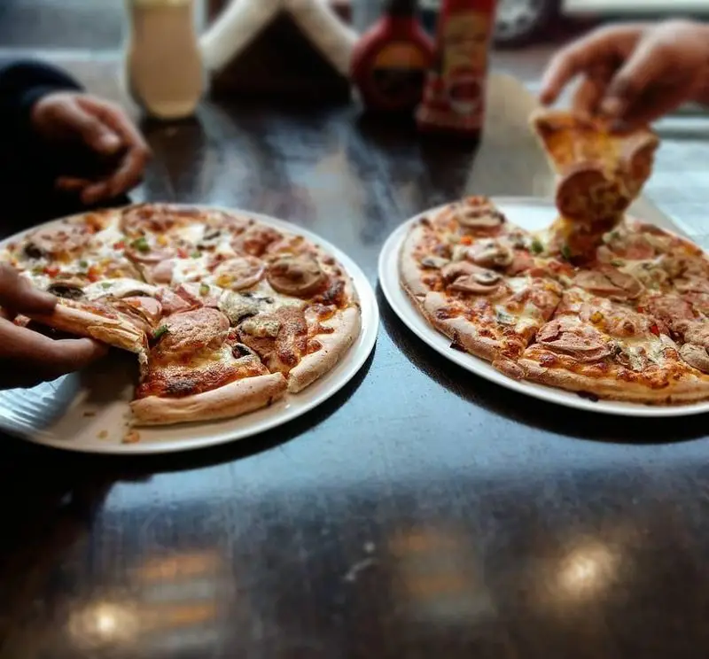 دو پیتزای داغ و خوشمزه رستوران گردسوز با پنیر کش‌دار، قارچ و سوسیس روی میز، آماده برای لذت بردن از طعم بی‌نظیر.