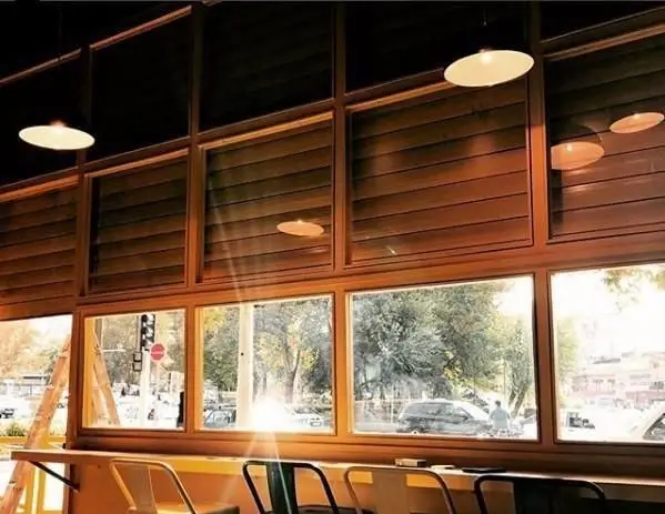 فضای داخلی دنج فست فود کیوسک برگر با پنجره‌های بزرگ چوبی، نور طبیعی و منظره زیبای شهری برای تجربه غذایی دلنشین.