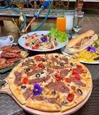 تصویری از میز غذا و نوشیدنی های متنوع در کافه رستوران سوته دلان: پیتزا، ساندویچ، سالاد و قلیان در فضایی دلنشین