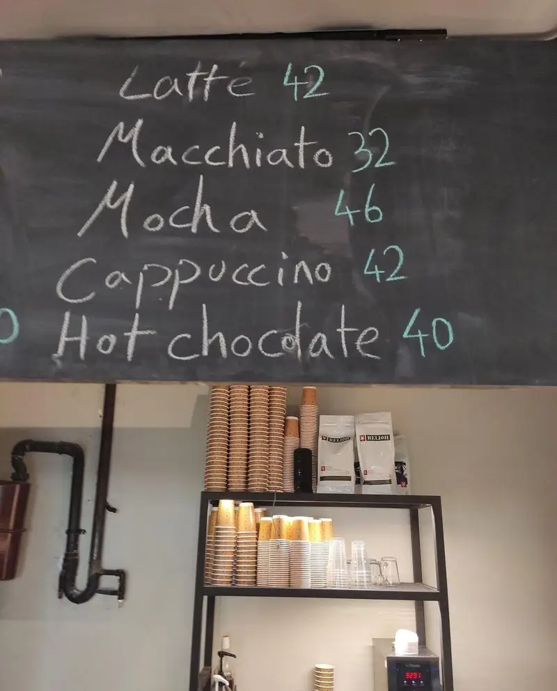 منوی نوشیدنی‌های گرم کافه نانوایی دوبار: لاته، ماکیاتو، موکا، کاپوچینو، هات چاکلت با قیمت. قفسه فنجان یکبار مصرف و بسته‌های قهوه.