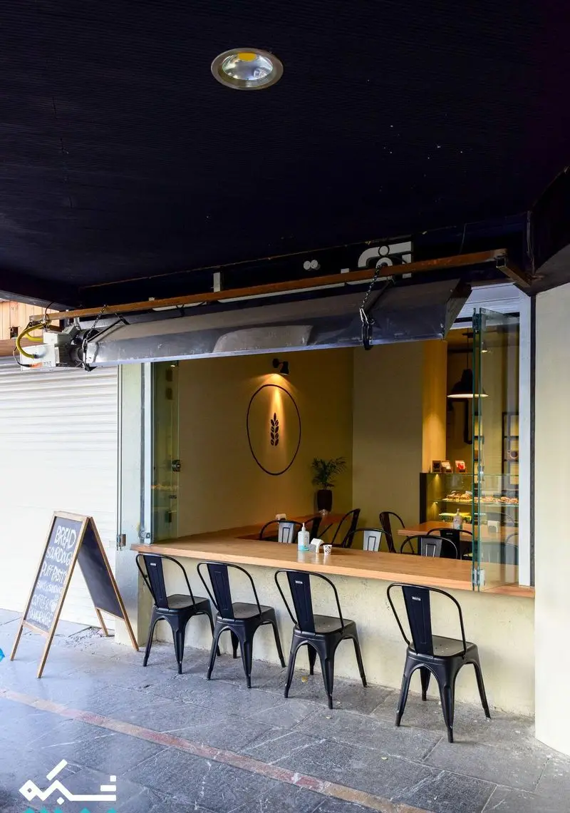 کافه نانوایی دوبار، نمای بیرونی با صندلی‌های مشکی و پیشخوان چوبی، ایده‌آل برای صرف نان تازه، شیرینی و قهوه در فضای باز.