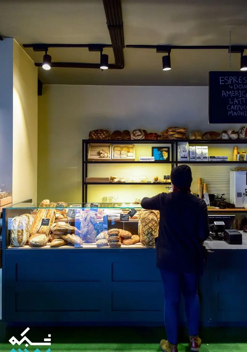 نمایی از کافه نانوایی دوبار با پیشخوان پر از نان‌های تازه، باگت‌های خوش‌رنگ و شیرینی‌های دست‌ساز در فضایی گرم و دنج.
