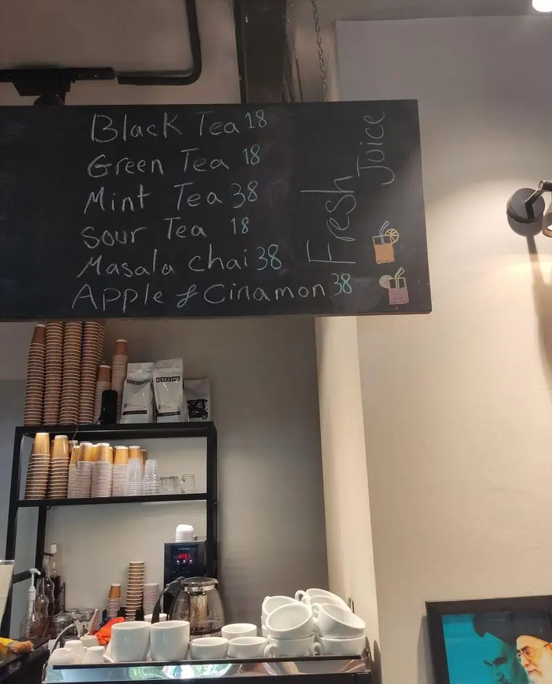 منوی چای و آبمیوه کافه نانوایی دوبار با لیست قیمت، شامل چای سیاه، سبز، نعناع، ترش، ماسالا و سیب و دارچین به همراه لیوان‌ها و لوازم سرو.