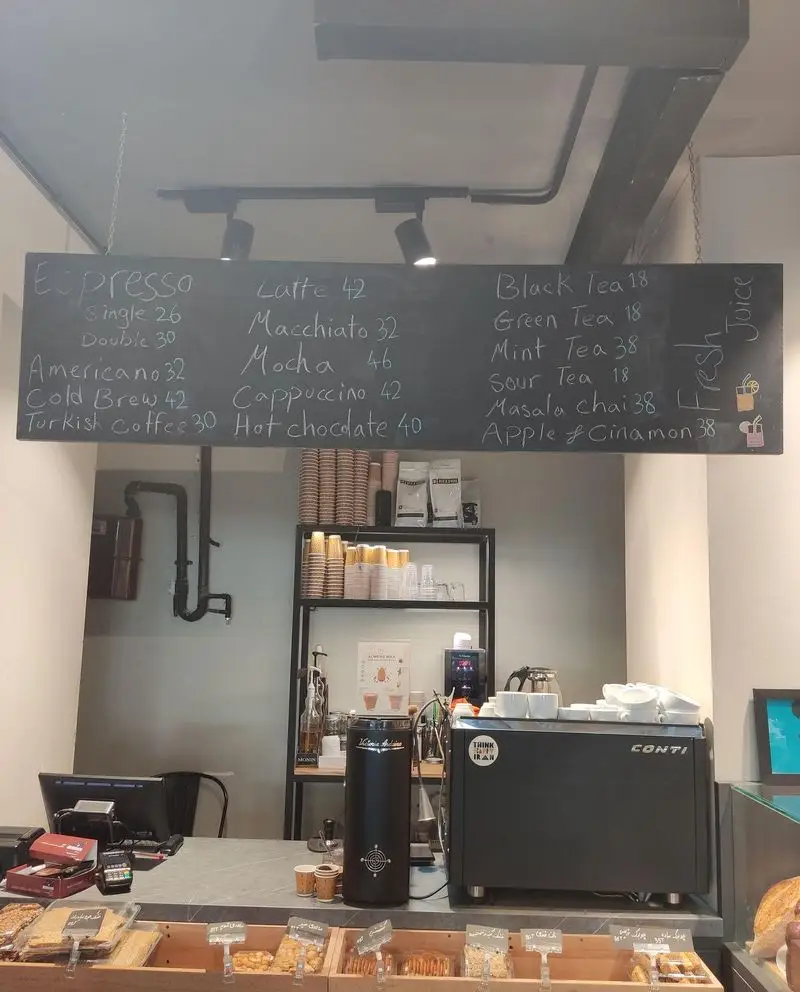 فضای دلنشین کافه نانوایی دوبار: منوی کامل قهوه، چای و آبمیوه روی تخته سیاه، به همراه دستگاه قهوه‌ساز و شیرینی‌های تازه.