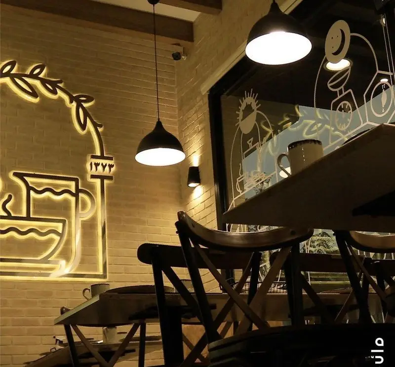 فضای داخلی مدرن و دنج کباب سرای مائده، با دیوارهای آجری، نورپردازی گرم، میز و صندلی‌های چوبی و نشانه نئونی ۱۳۷۳.