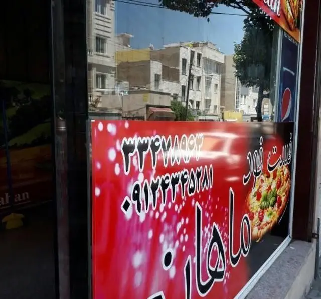 نمایی از تابلوی جذاب فست فود ماهان با لوگوی پیتزای خوشمزه و شماره تلفن های ضروری ۳۳۳۶۷۸۵۳ و ۰۹۱۲۴۳۳۲۵۲۸۱ برای سفارش آنلاین.