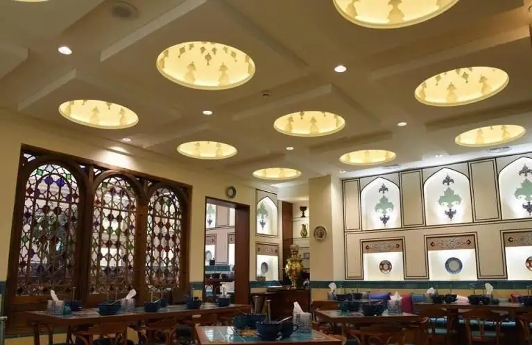 فضای داخلی دلنشین کافه رستوران پنج دری با پنجره‌های ارسی رنگی، سقف نورپردازی و دکوراسیون سنتی و چشم‌نواز ایرانی.