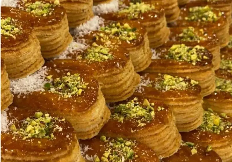 شیرینی‌های باقلوای نازگل با لایه‌های ترد و روکش عسلی، تزئین شده با پسته و نارگیل، آماده برای سفارش از شیرینی و قنادی نازگل.