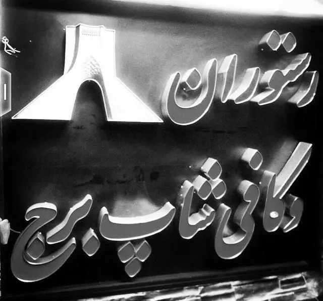 تصویر تابلوی کافه رستوران برج آزادی تهران با حروف فارسی برجسته سفید، نشانگر خدمات رستوران، کافی شاپ و لوگوی برج آزادی.