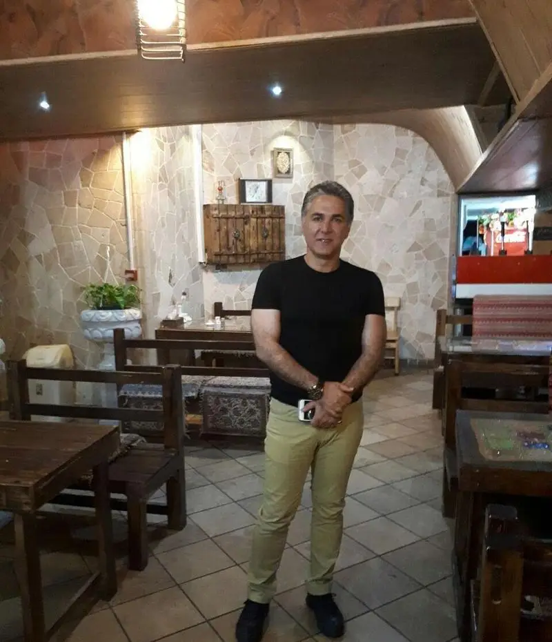 تصویری از یک مرد در فضای داخلی دلنشین کافه رستوران برج آزادی با دکوراسیون سنگی، میز و صندلی‌های چوبی و نورپردازی گرم.