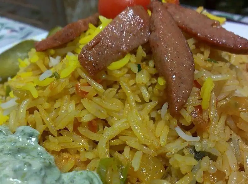 سوسیس گریل شده روی پلو زعفرانی و برنج رنگین کافه رستوران برج آزادی، همراه با سس مخصوص و ترشی، یک وعده غذایی دلچسب و کامل.