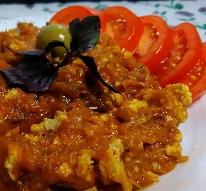 خوراک گرم و خوش‌طعم با سس گوجه‌فرنگی، تخم‌مرغ و سبزیجات معطر، همراه با برش‌های تازه گوجه و زیتون، در کافه رستوران برج آزادی.