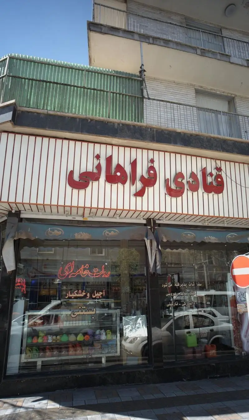 تصویر نمای بیرونی قنادی فراهانی با تابلو قرمز روشن، ویترین شیشه‌ای پر از شیرینی، رولت، آجیل، خشکبار و بستنی.