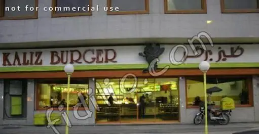تصویری از نمای خارجی فست فود کالیز برگر، یک رستوران با تابلوی مشخص، فضای داخلی روشن و موتورسیکلت تحویل غذا در پیاده‌رو.