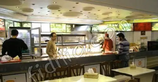 تصویری از فضای داخلی تمیز و روشن فست فود کلیز، شامل پرسنل در حال خدمت‌رسانی پشت پیشخوان و محیط دلنشین برای مشتریان.