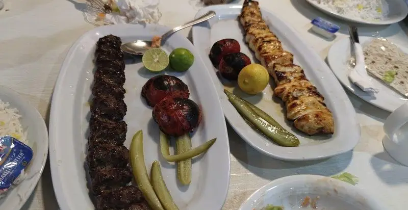 میز غذای دلنشین رستوران افتخاری شامل کباب کوبیده و جوجه کباب طلایی با برنج، گوجه کبابی، لیمو تازه و خیارشور. تجربه غذای لذیذ ایرانی.