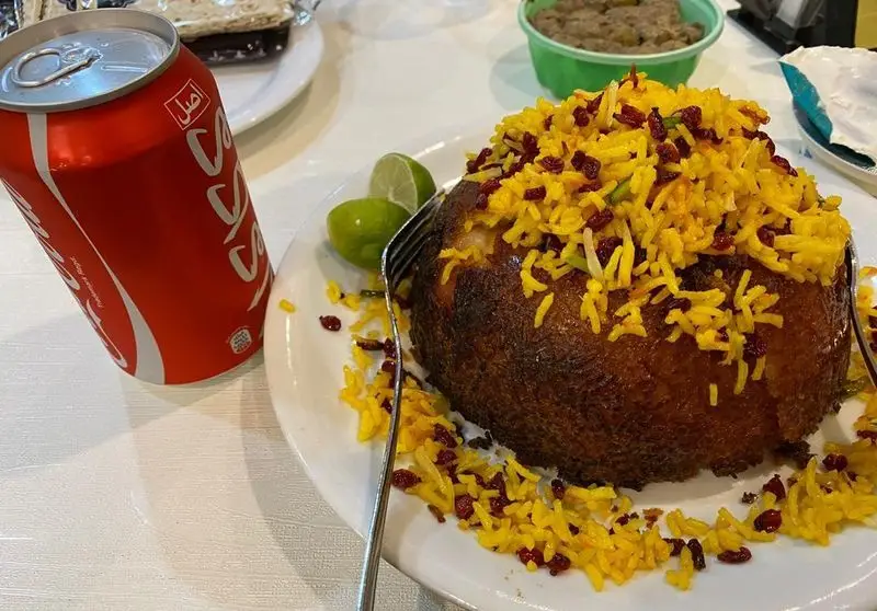 غذای خوشمزه و زیبای رستوران افتخاری: برنج زعفرانی با زرشک و ته دیگ، همراه با نوشابه کوکاکولا. تجربه‌ای لذیذ از غذای ایرانی.