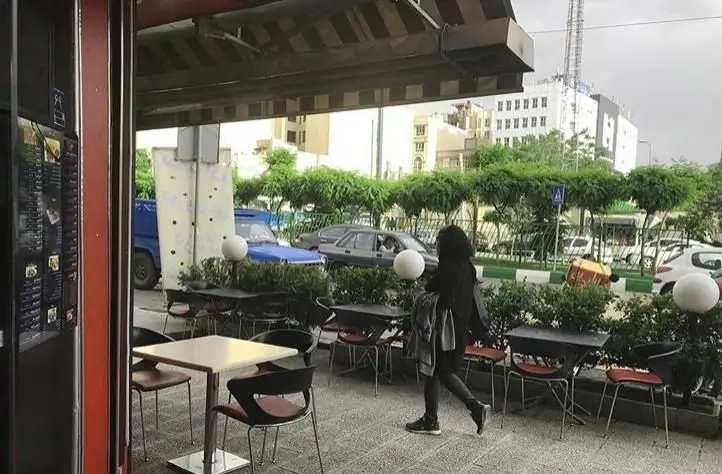 نمای دلنشین فضای باز رستوران سنتی علاالدین با میز و صندلی‌های آماده برای پذیرایی مشتریان، در کنار خیابانی پردرخت و شهری.