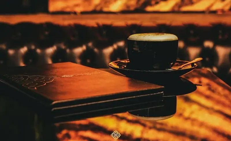 تصویری از میز کافه رستوران ایرانی شاندیز ماهان رویال: فنجان قهوه، منوی طرح‌دار و فضایی دنج و گرم مناسب برای شب‌ها.